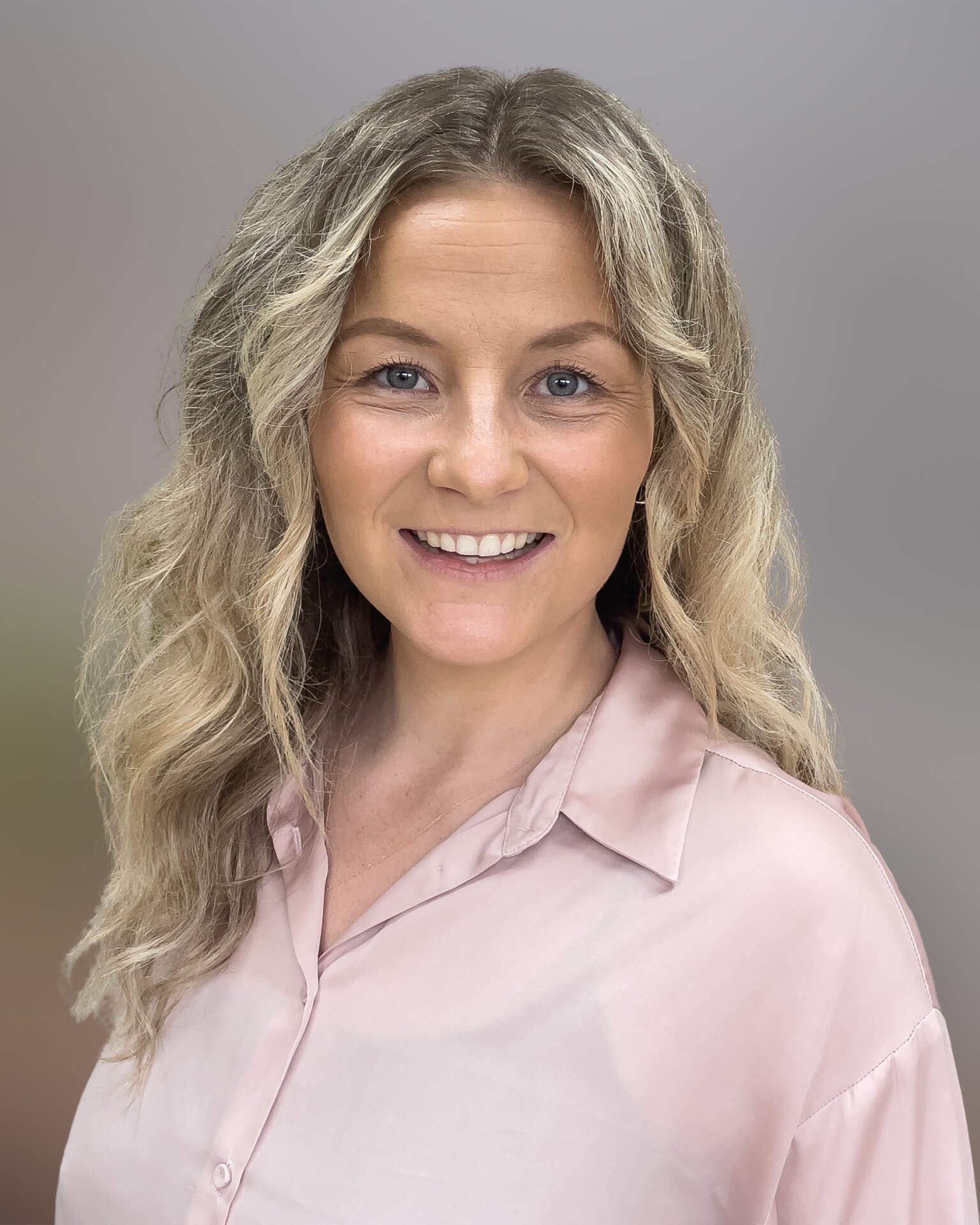 Headshot of Elona Smith, wearing a pink shirt with her blonde, curly hair down