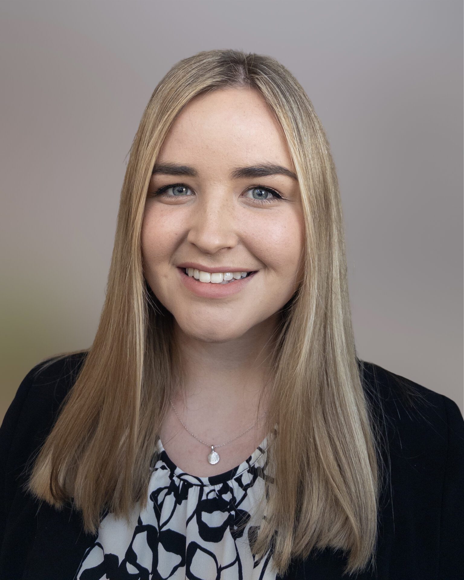 Headshot of Ellie Chivers, wearing a patterned top on a grey background