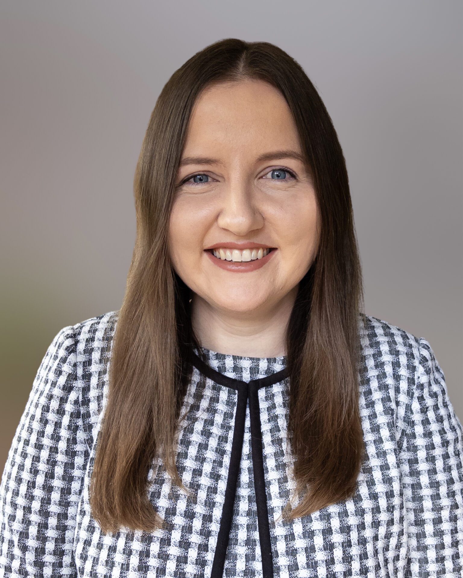 Headshot of Beth Duffy, wearing a black and white gingham blouse with her brown hair down